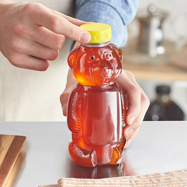 A person holding a 16 oz. Bear PET honey bottle with a yellow flip top lid full of honey.