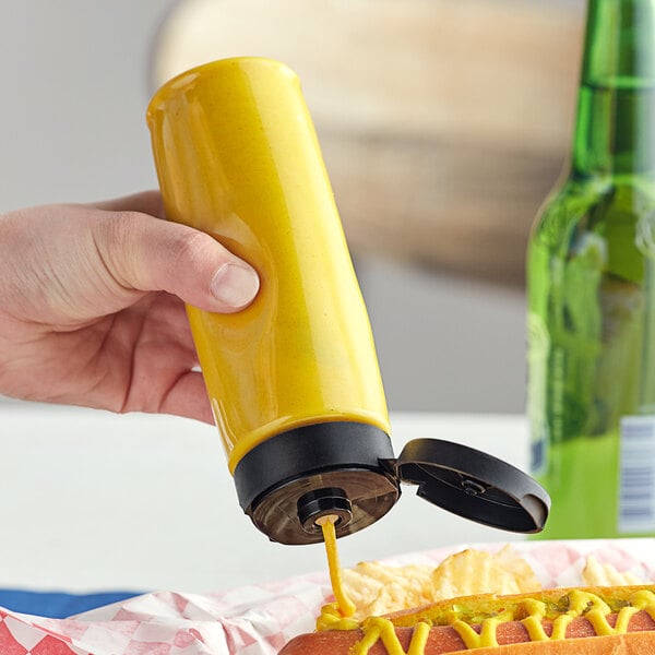A hand using a yellow squeeze bottle to pour mustard onto a hot dog.