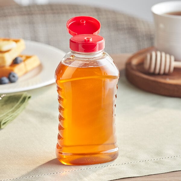 An 11 oz. ribbed hourglass PET honey bottle with a red cap on a table with pancakes.