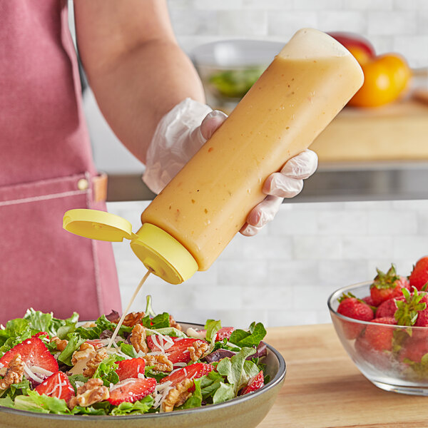 A person's hand holding a yellow cylinder bottle with yellow liquid pouring onto a salad.