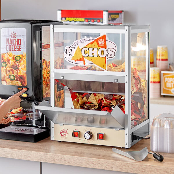 A woman using a Carnival King countertop nacho warmer to fill a bowl with chips.