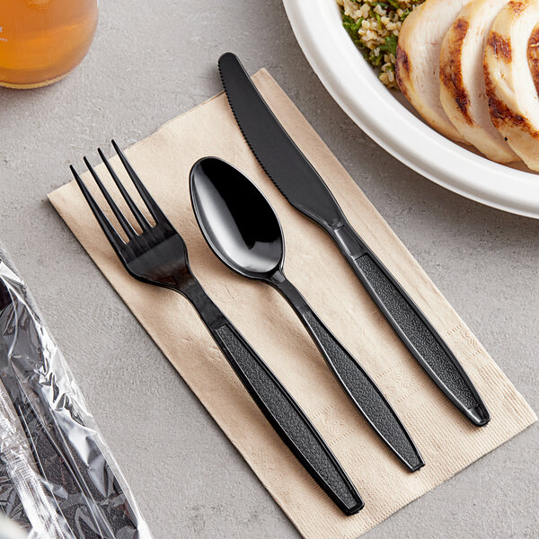 A black spoon, fork, and knife on a napkin.