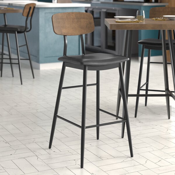 A Lancaster Table & Seating black barstool with a black vinyl seat and wood backrest.