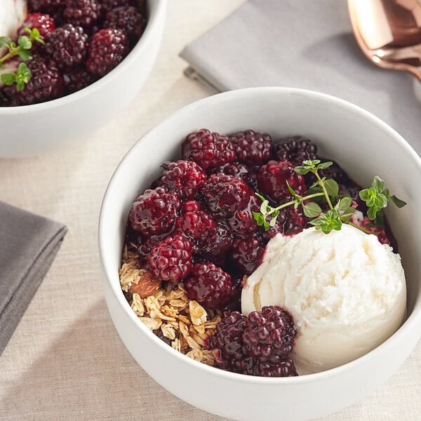A bowl of ice cream with whole blackberries next to a bowl of whole blackberries.
