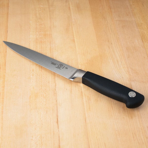 A Mercer Culinary Genesis forged flexible fillet knife with a black handle on a wooden table.