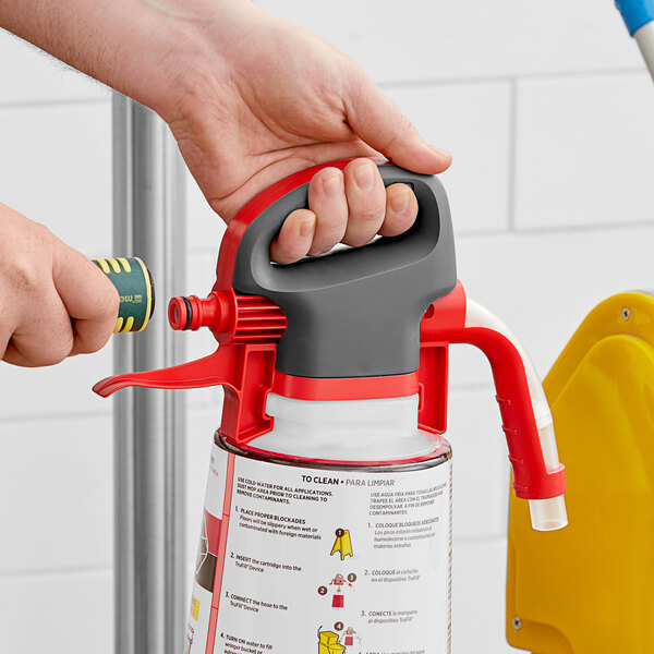 A hand holding a red and black plastic SC Johnson Professional TruFill dispenser head sprayer.