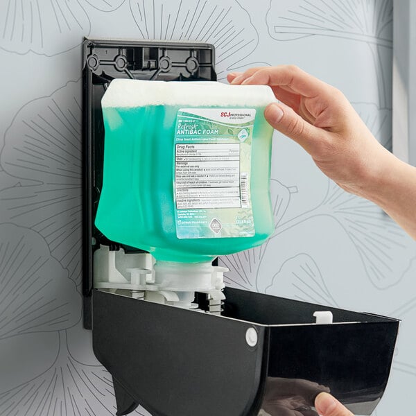 A hand holding a SC Johnson Professional Refresh Antibacterial Foaming Hand Soap Refill container with blue liquid.