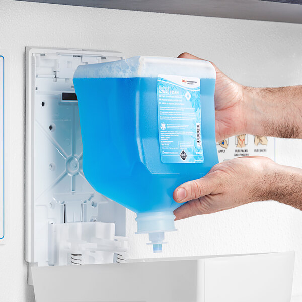 A person holding a SC Johnson Professional Refresh Azure Foaming Hand Soap refill container of blue liquid.