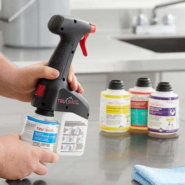 A person using a SC Johnson Professional TruShot 2.0 spray gun to dispense liquid from a black and blue bottle over a counter.