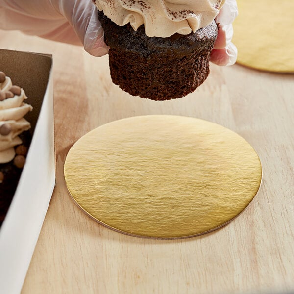 A hand holding a chocolate cupcake on a gold Enjay dessert board.