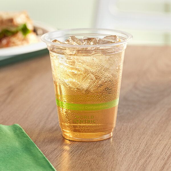A World Centric compostable plastic cup with ice and liquid on a table.