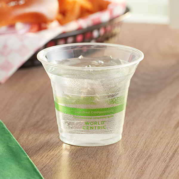 A clear World Centric plastic cup filled with ice water on a table.