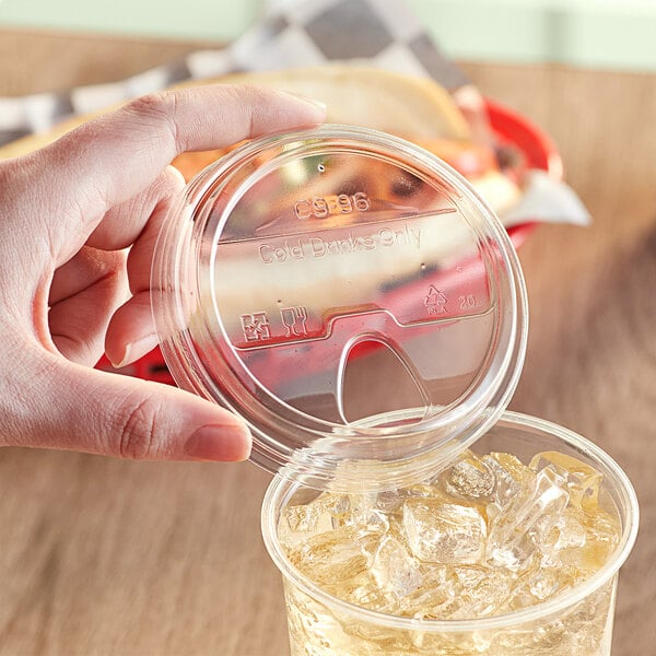 A hand placing a World Centric PLA plastic lid on a clear cup of ice.