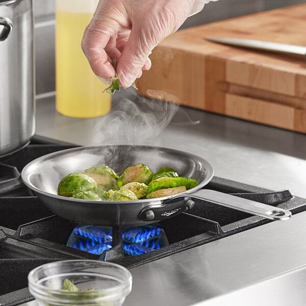 A person cooking brussels sprouts in a Vollrath stainless steel fry pan on a stove.