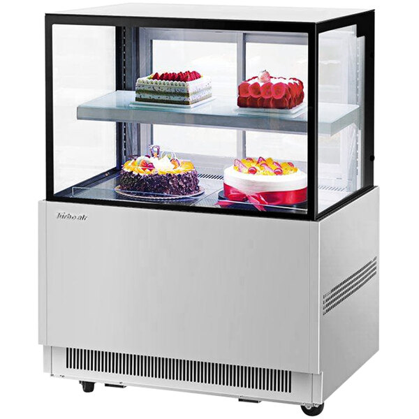 A Turbo Air refrigerated bakery display case with cakes on two tiers behind glass.