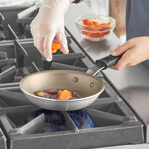 A person using a Vollrath Wear-Ever aluminum non-stick fry pan to cook carrots on a stove.