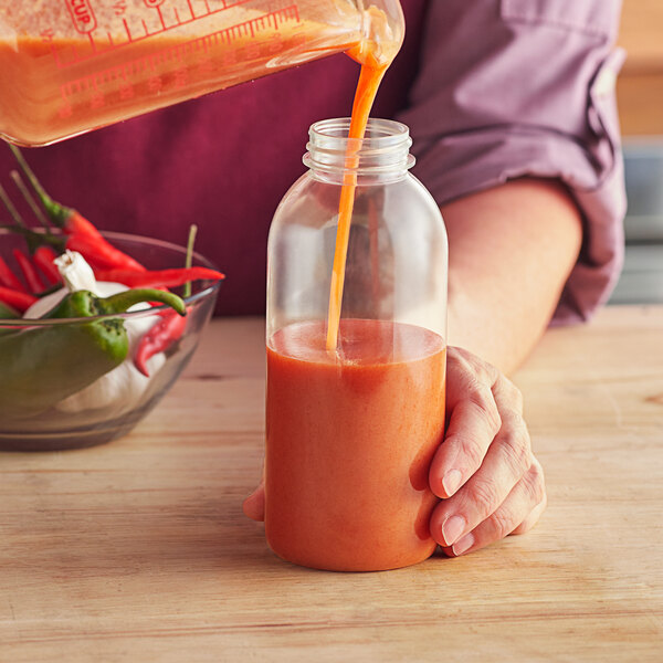 A person pouring orange liquid into a 12 oz. PET round sauce bottle.