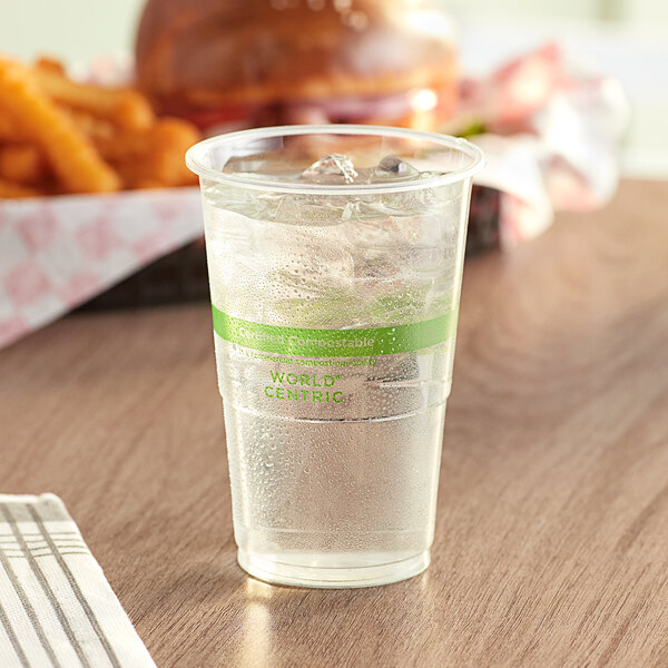 A clear World Centric plastic cup with ice and water on a table.