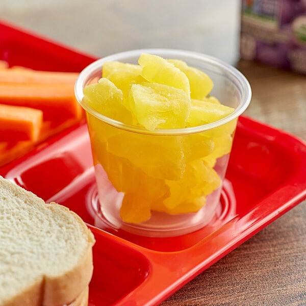 A plastic cup of dehydrated pineapple chunks on a tray.