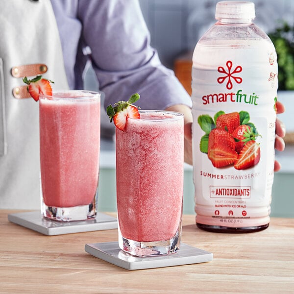A person holding a bottle of Smartfruit Summer Strawberry Puree next to a glass of strawberry smoothie.