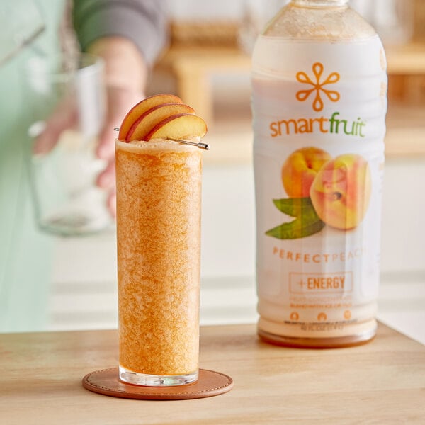 A glass of Smartfruit Perfect Peach smoothie on a table with a peach on top.