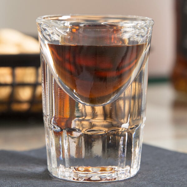 A Libbey tall shot glass with a shot of brown liquor.