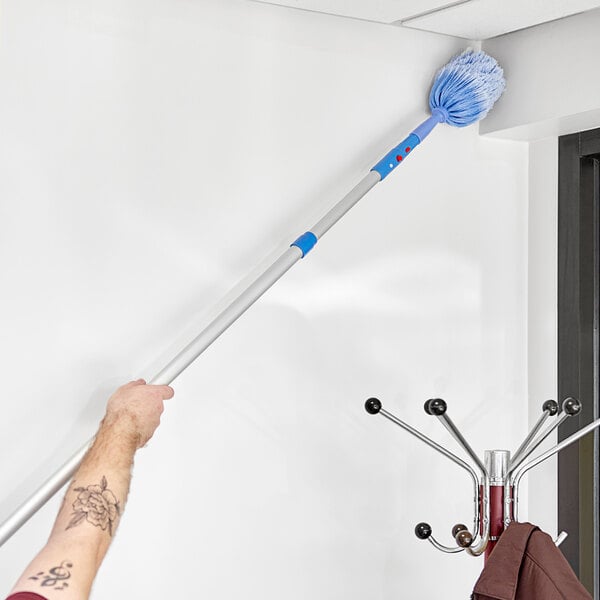 A person using a Lavex telescopic duster to clean a corner.