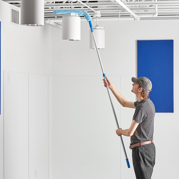 A man using a Lavex 24" Flex Wand Duster with Microfiber Sleeve to clean the ceiling.