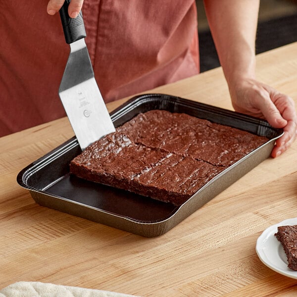 A woman using a spatula to cut a brownie in a Solut Bake and Show black sheet pan.