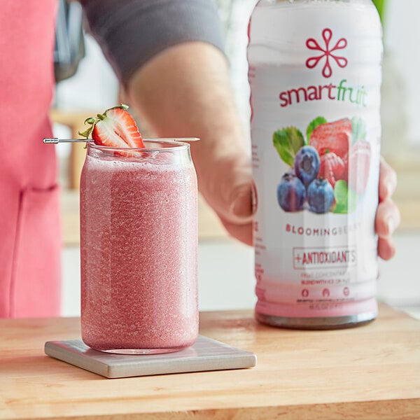 A person holding a jar of Smartfruit Blooming Berry Puree next to a glass of pink liquid.