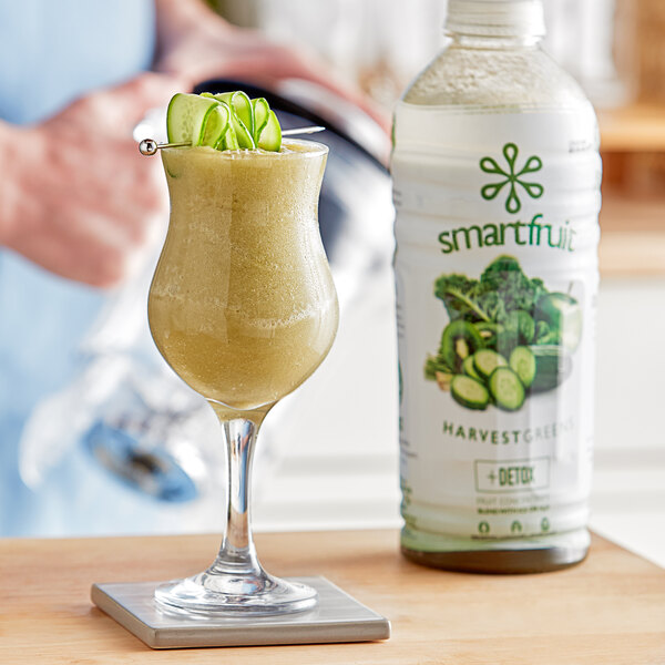 A person holding a glass of green Smartfruit Harvest Greens smoothie.