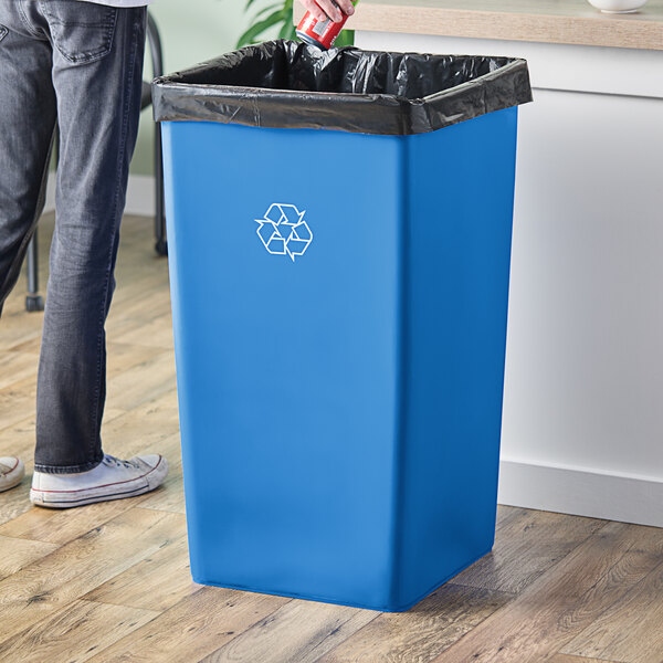 A man putting a black trash bag into a blue Lavex square recycling can.