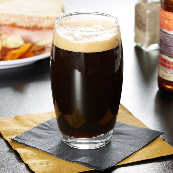 A glass of dark beer on a table with a sandwich.