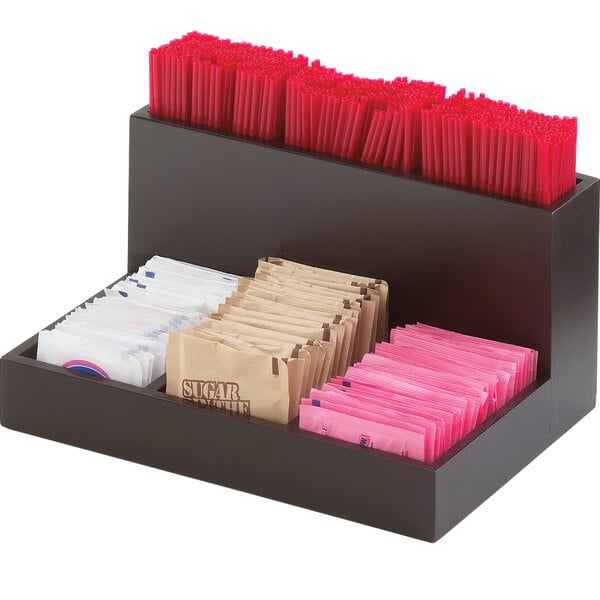 A black bamboo organizer with sugar packets and straws on a counter.