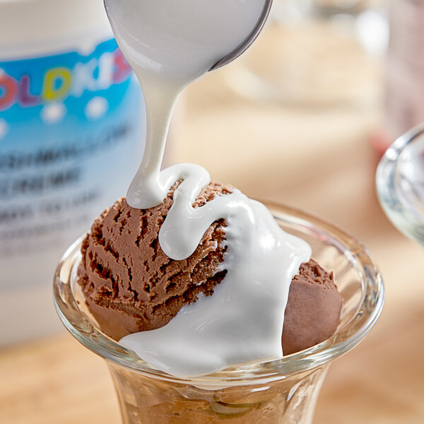 A spoon pouring Koldkiss Marshmallow snowball creme topping onto a scoop of ice cream.