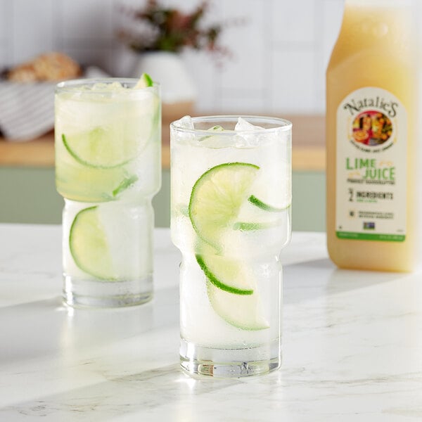 A pair of glasses with ice, lime slices, and Natalie's Lime Juice on a table.