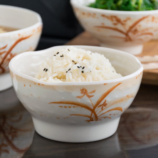 A close up of a Thunder Group Gold Orchid melamine wave rice bowl filled with rice and greens.