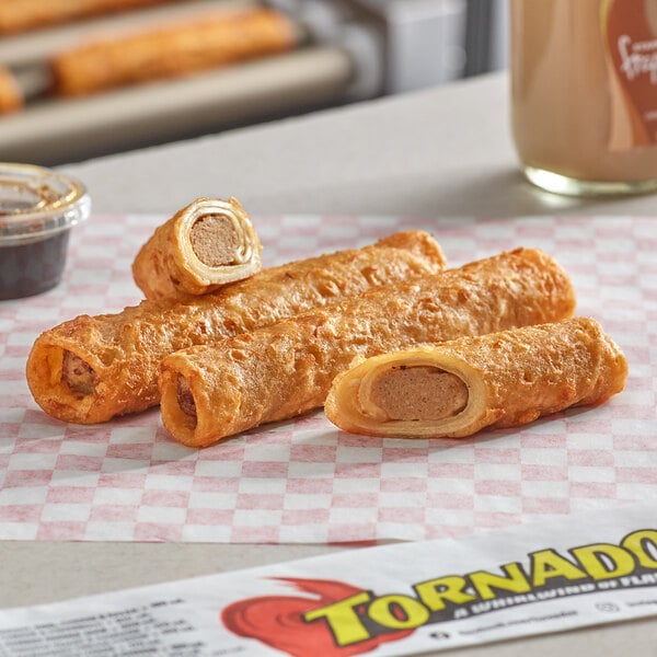 A close-up of Ruiz Foods French Toast & Sausage Tornado taquitos on a checkered paper.
