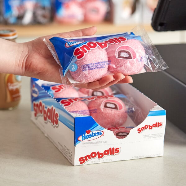 A hand holding a pink package of Hostess Snoball cakes.