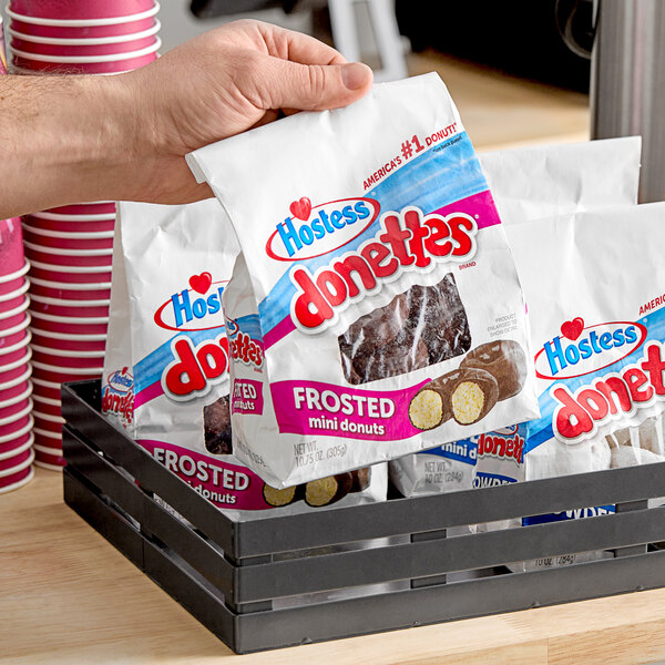 A hand holding a bag of Hostess chocolate frosted mini donuts.