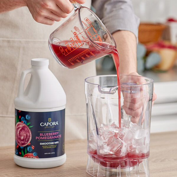 A person pouring Capora Blueberry Pomegranate smoothie mix into a blender.