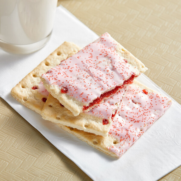 A stack of Pop-Tarts Frosted Cherry crackers with pink frosting next to a glass of milk on a napkin.