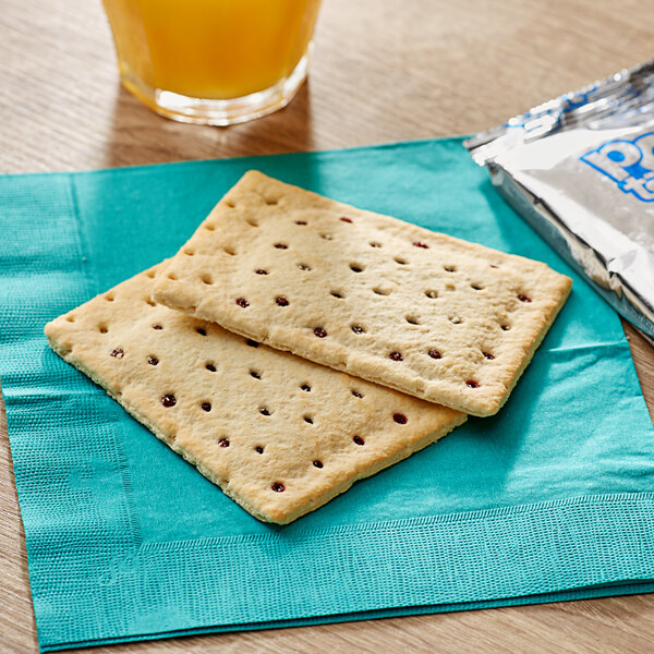 Two unfrosted blueberry Pop-Tarts on a napkin next to a glass of juice.