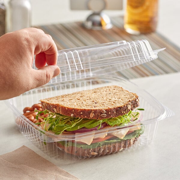 A hand holding a sandwich in a Stalk Market clear plastic container.