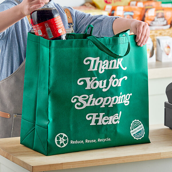 A woman putting a bottle of soda into a green RediBag USA reusable shopping bag.