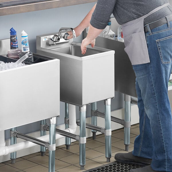 A person standing next to a Steelton underbar hand sink on a counter in a professional kitchen.