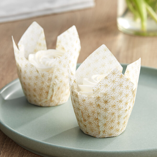 Two Baker's Mark tulip cupcake wrappers with a white background and gold print.