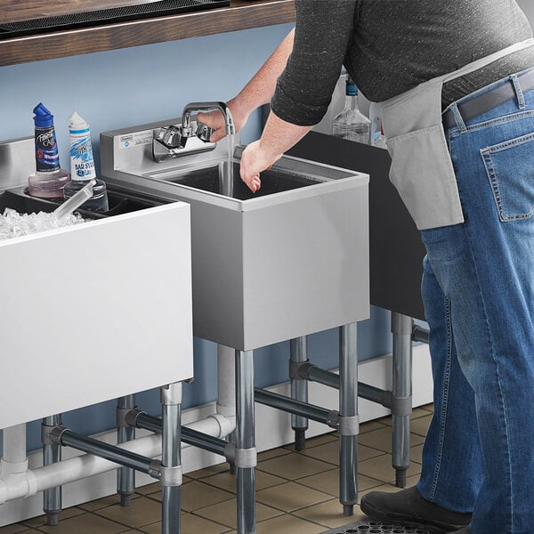 A man in a black shirt and blue jeans standing next to a Steelton underbar dump sink on a counter in a professional kitchen.