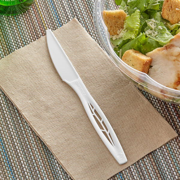 A white Stalk Market CPLA knife on a napkin next to a bowl of salad.