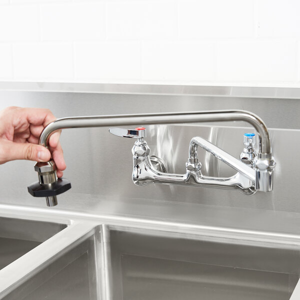 A hand holding a T&S pot filler faucet over a stainless steel sink.